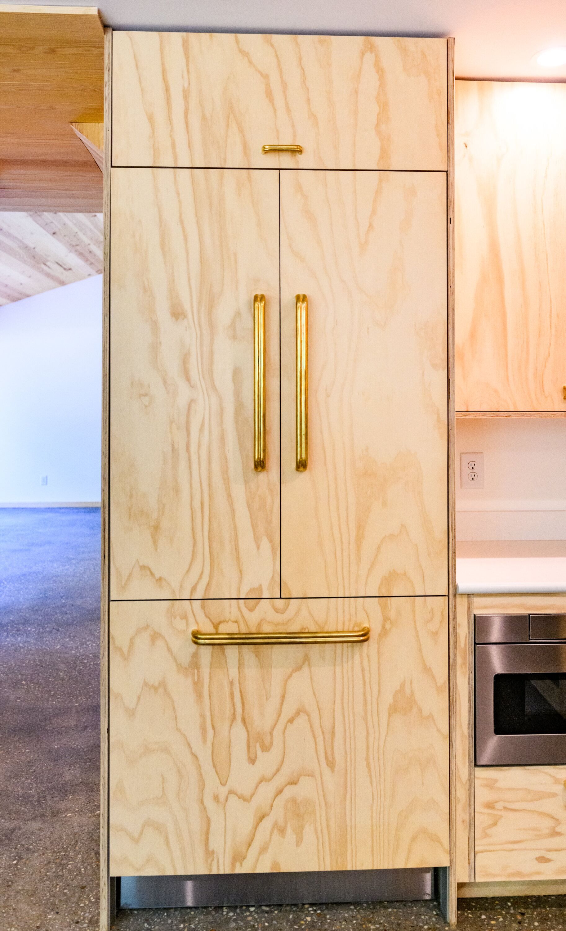 Tall cabinet run in locally milled wood with brass pulls and a panel front refrigerator