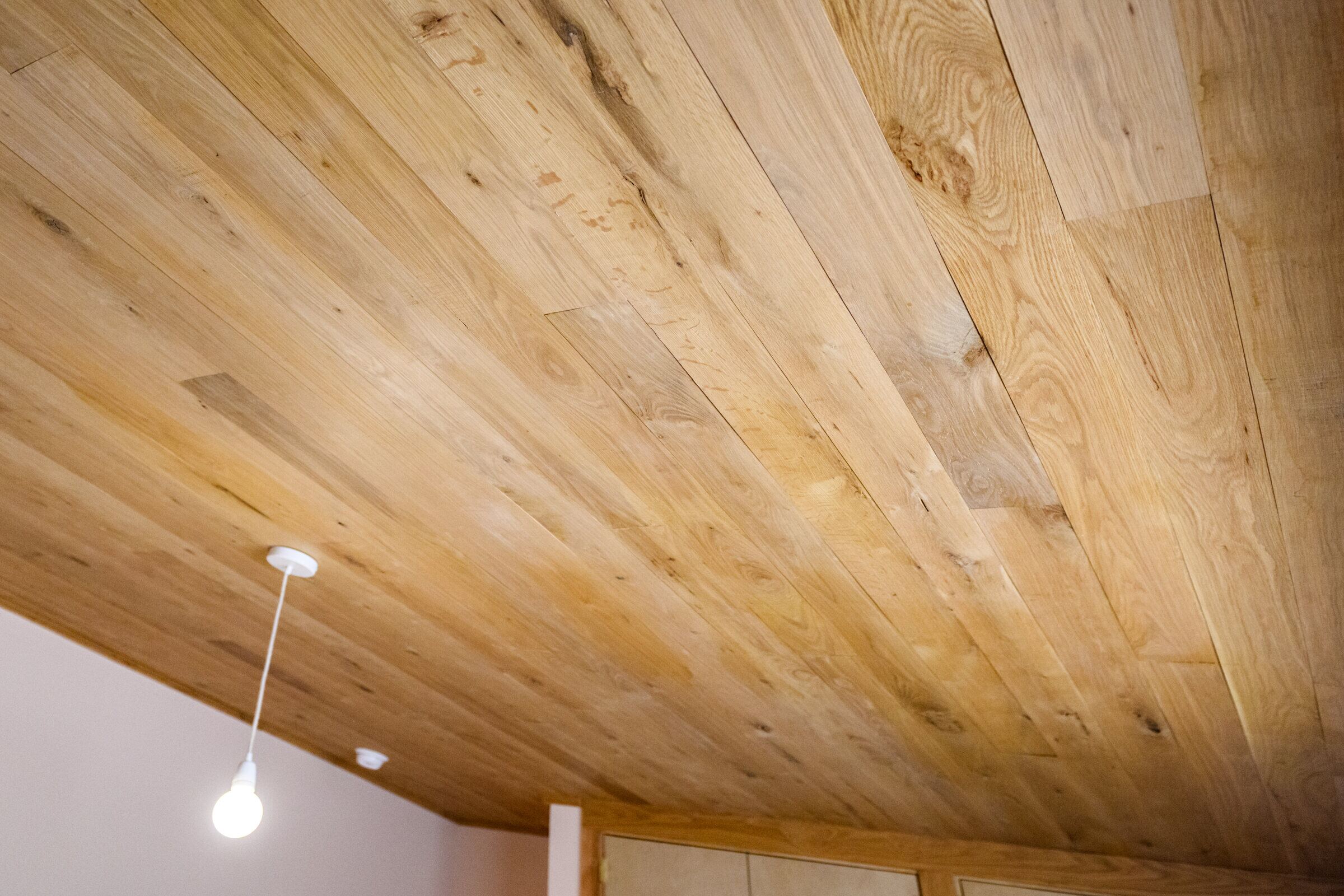 Wood plank ceiling following the roof pitch with pendant lighting