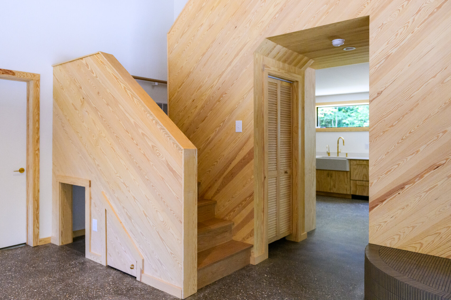 Sculptural stair volume clad in locally milled wood with a hidden storage door